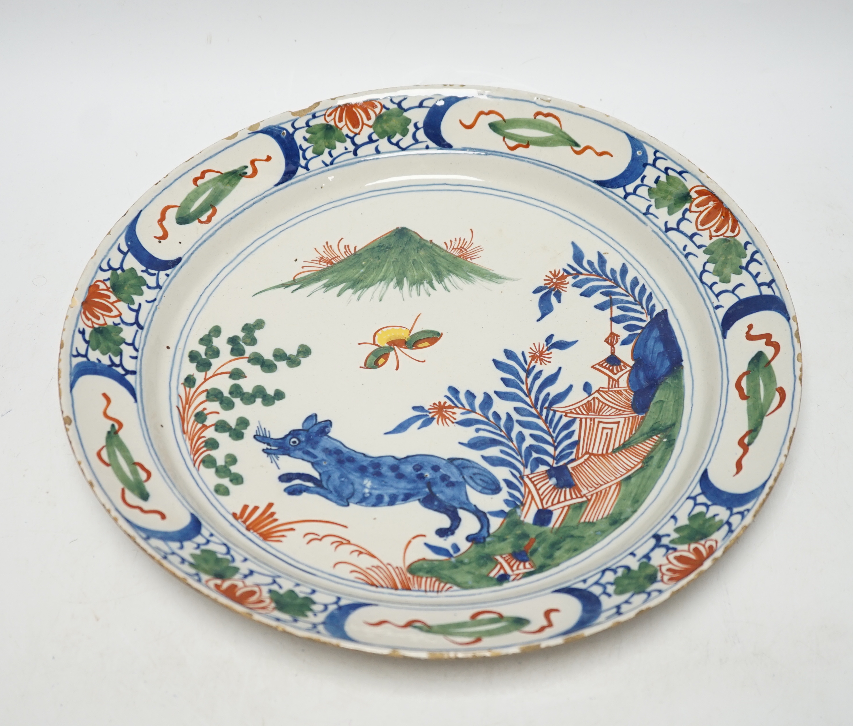 An 18th century Delft dish, the centre painted with a wolf, a bee and a pavilion, 35cm